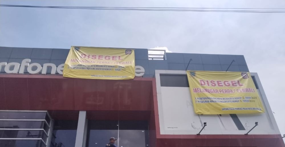 TAK BERIZIN: Petugas Satpol PP Kota Mojokerto memasang spanduk segel di reklame toko Erafone & More di Jalan Gajah Mada, kemarin (9/1).