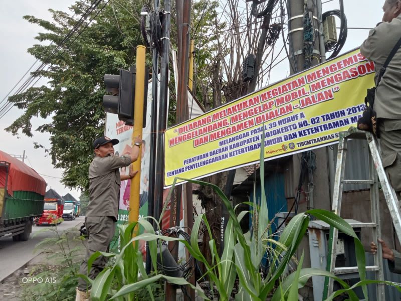 PREVENTIF: Petugas Satpol PP Kabupaten Mojokerto memasang spanduk imbauan di sejumlah titik persimpangan rawan PMKS, kemarin.