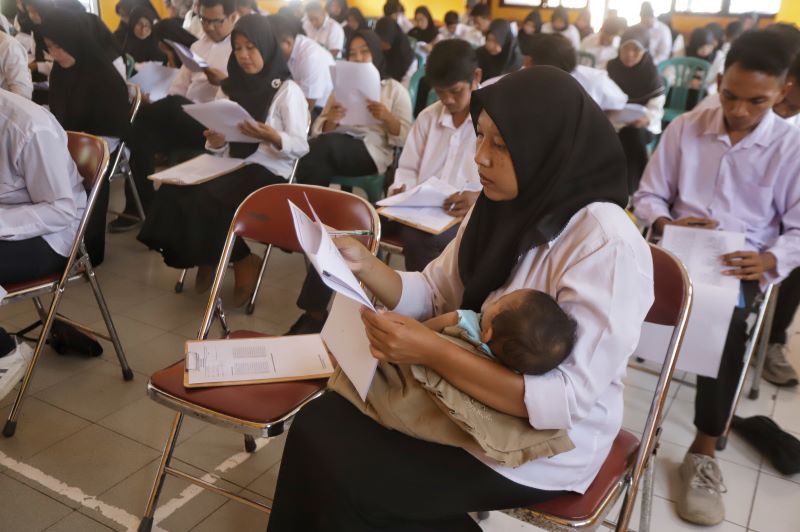 DEMI KELULUSAN: Lia Ratnasari, salah satu warga belajar UPT SKB Gedeg Mojokerto saat mengerjakan ujian pendidikan kesetaraan sambil menggendong buah hatinya.&nbsp;