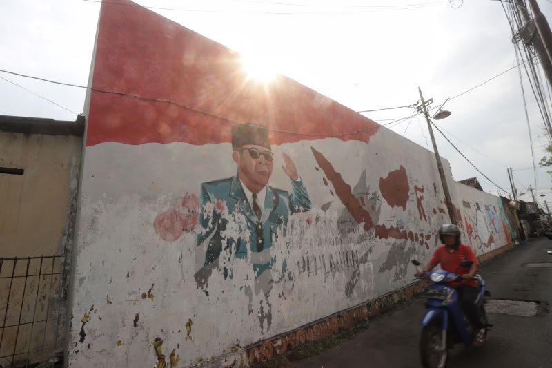 MURAL: Warga melintas di depan mural dinding bergambar Presiden RI pertama Soekarno di Kelurahan Purwotengah, Kecamatan Kranggan, Kota Mojokerto kemarin (17/6).