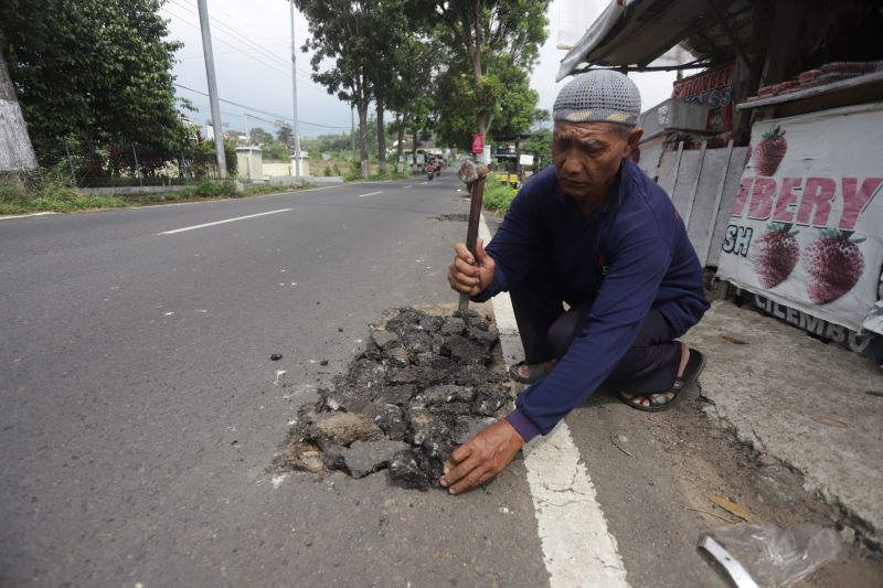 RAWAN LAKA: Darman, warga setempat terpaksa menambal lubang bekas galian pencurian kabel di ruas Jalan Pacet-Gondang, Desa Sajen, Kecamatan Pacet, Kabupaten Mojokerto, kemarin (19/6).