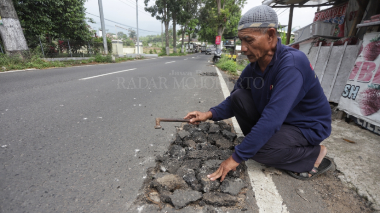 SWADAYA: Darman, 70, penjual stroberi menambal lubang bekas galian pencurian kabel yang membahayakan pengguna Jalan Raya Pacet-Gondang, Kabupaten Mojokerto, Kamis (19/6).