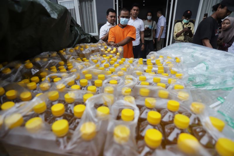 ILEGAL: Nur Suhadi Yanto bersama barang bukti minyak goreng curah kemasannya saat dirilis Polres Mojokerto Kota, Maret lalu.