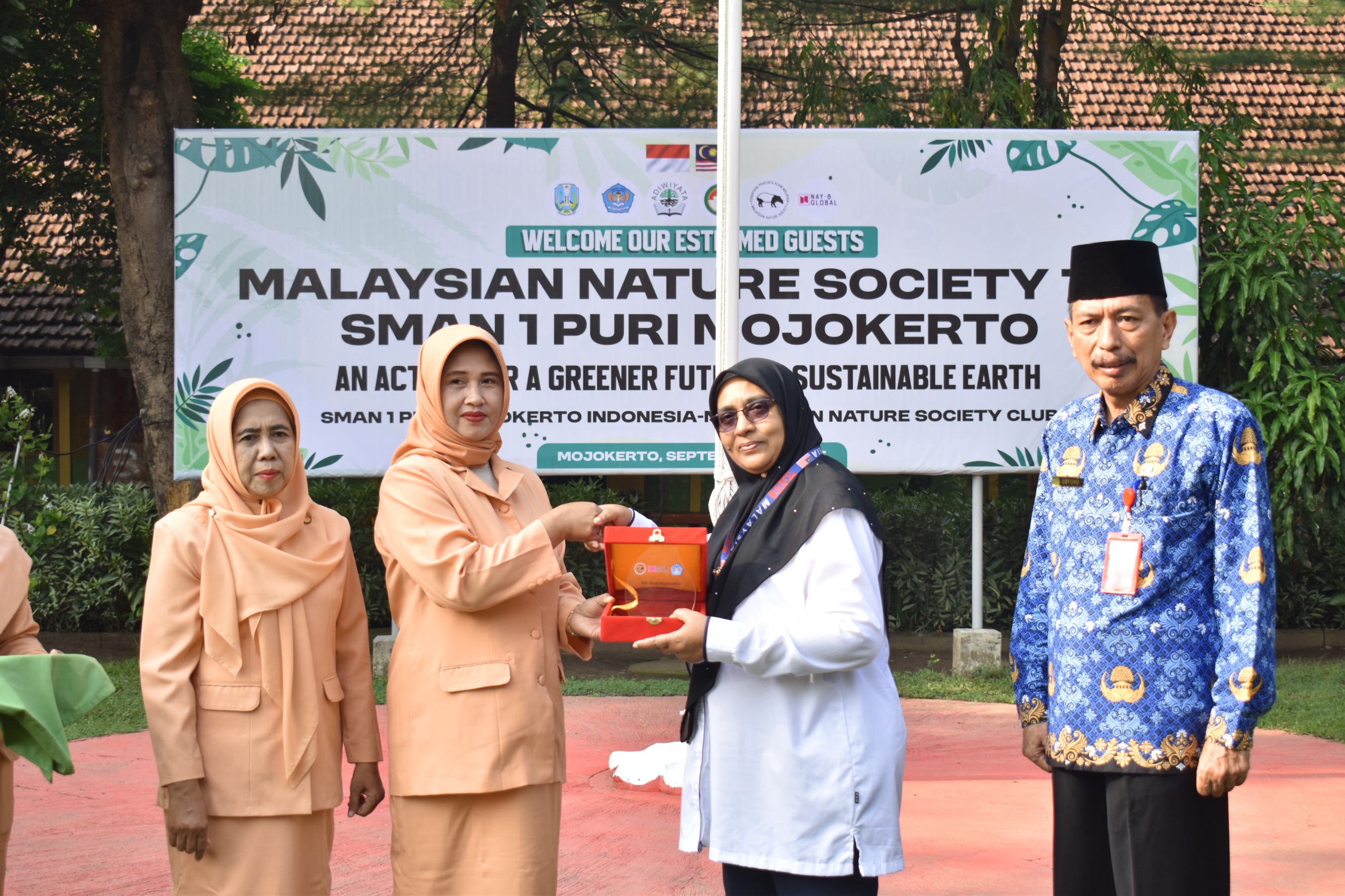 ketua Darma Wanita Cabdin Mojokerto Endang Mudianto bersama Ketua Darma Wanita SMAN 1 Puri Aliyah Sutoyo menyerahkan dan menerima cenderamata dari kepala sekolah Negeri Malaysia.