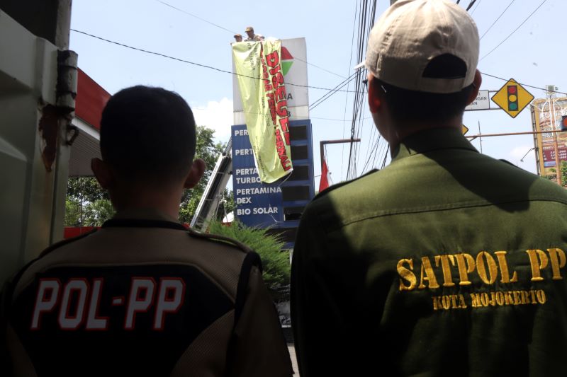 BERMASALAH: Petugas memasang tanda segel pada reklame papan nama SPBU Pertamina Gajah Mada di Jalan Gajah Mada, Kota Mojokerto, kemarin (25/9).