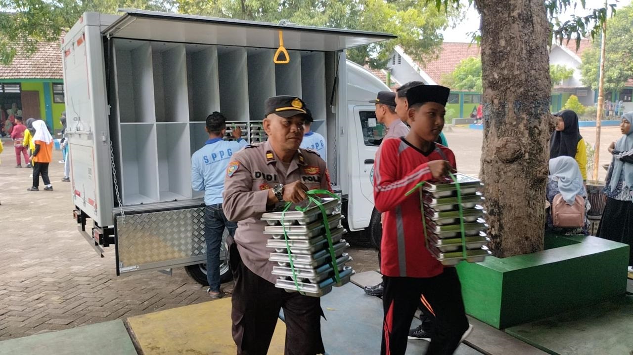 DIPERKETAT: Petugas SPPG saat mendistribusikan MBG kepada pelajar dan santri dengan dikawal petugas kepolisian dan TNI di Trowulan pada Agustus lalu.
