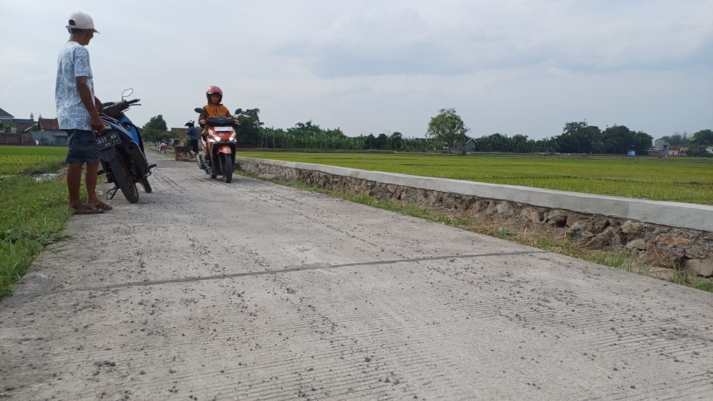 INFRASTRUKTUR: Pengguna roda dua melintas di jalan penghubung antar desa yang baru dibangun, lengkap dengan tembok penahan tanah (TPT) yang tampak kokoh.