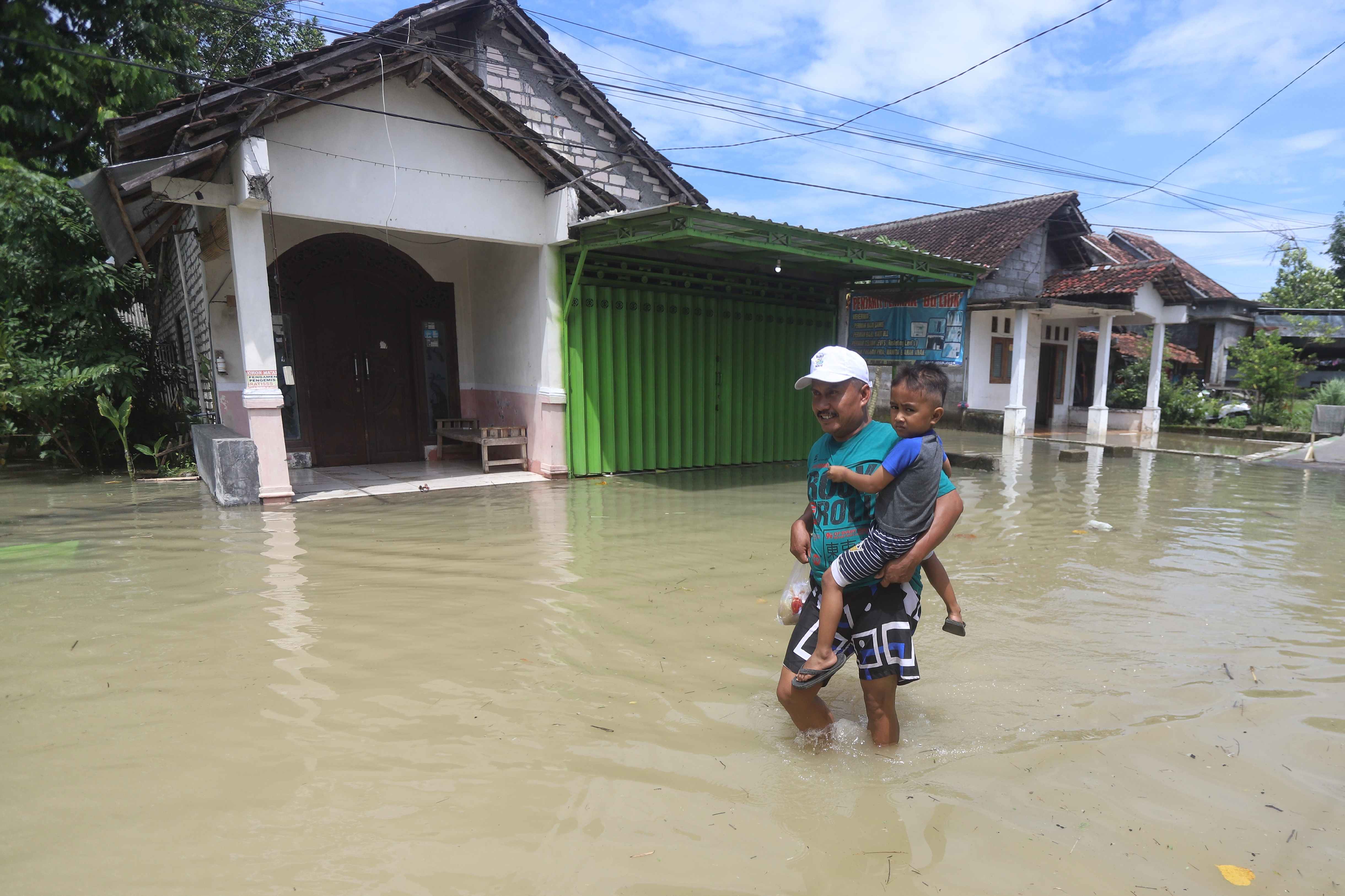 TERENDAM: Warga Dusun Klanting, Desa Pulorejo, Kecamatan Dawarblandong, Kabupaten Mojokerto melintasi jalan yang tergenang, Senin (22/12).