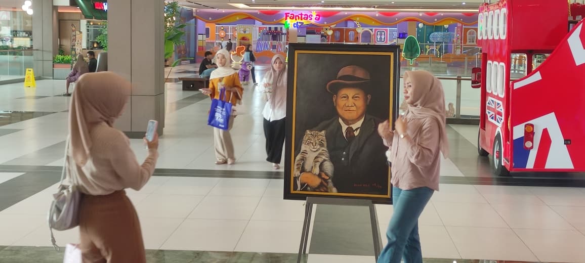 TERPIKAT: Pengunjung Sunrise Mall 2 Mojokerto mengamati dan berswafoto dengan lukisan Presiden Prabowo bersama kucingnya di pameran tunggal karya Diak Eko, kemarin (22/12).&nbsp;