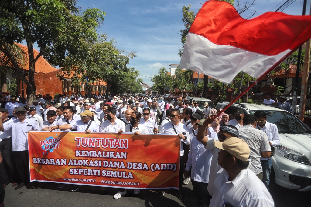 KIBARKAN MERAH PUTIH: Ratusan kades dan perangkat desa yang tergabung dalam Pamong Mojopahit membentangkan spanduk di kawasan Alun-Alun Wiraraja, Kota Mojokerto, sebelum menggelar long march menuju ka