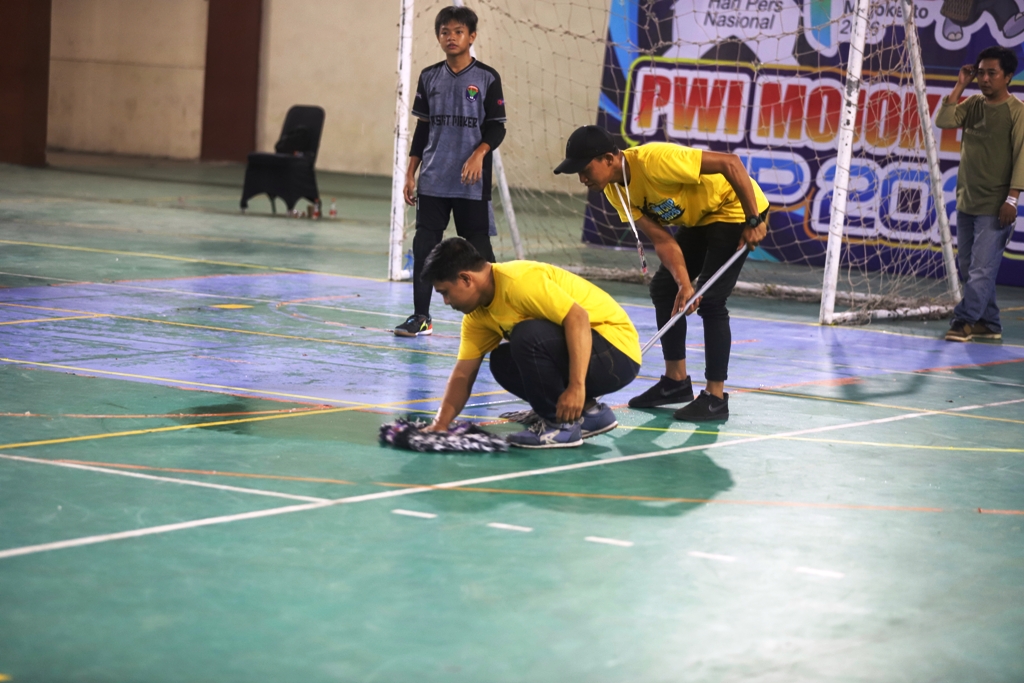 GANGGU PERTANDINGAN: Atap bocor GOR Seni Mojopahit Kota Mojokerto membuat lapangan futsal licin, Jumat (23/1). Panitia turnamen terpaksa mengelap agar pemain aman.