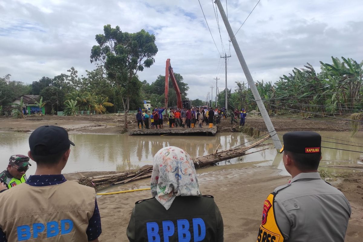 Aparat dan BPBD meninjau titik tanggul jebol yang menyebabkan akses jalan terputus dan permukiman tergenang.
