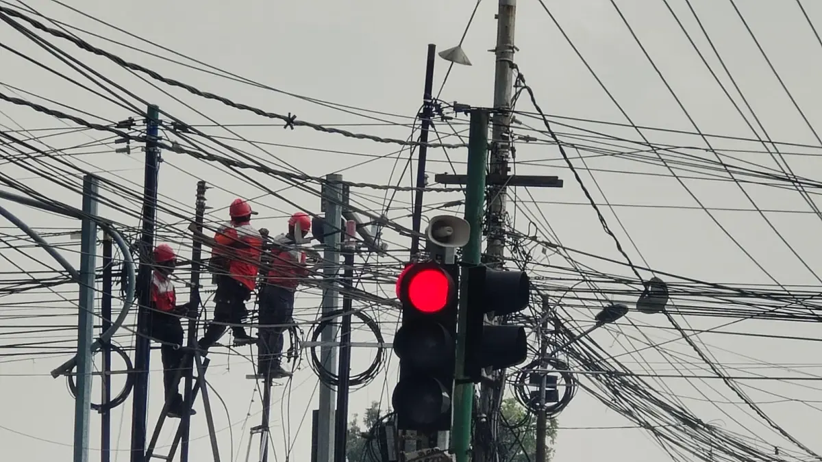 TAK BERATURAN: Tiang dan kabel FO di perempatan Jalan RA Basuni, Desa/Kecamatan Sooko tampak semrawut. Banyaknya pemasangan tiang FO diduga tak berizin ini turut menjadi atensi DPRD dan eksekutif. (Dori JPRM)