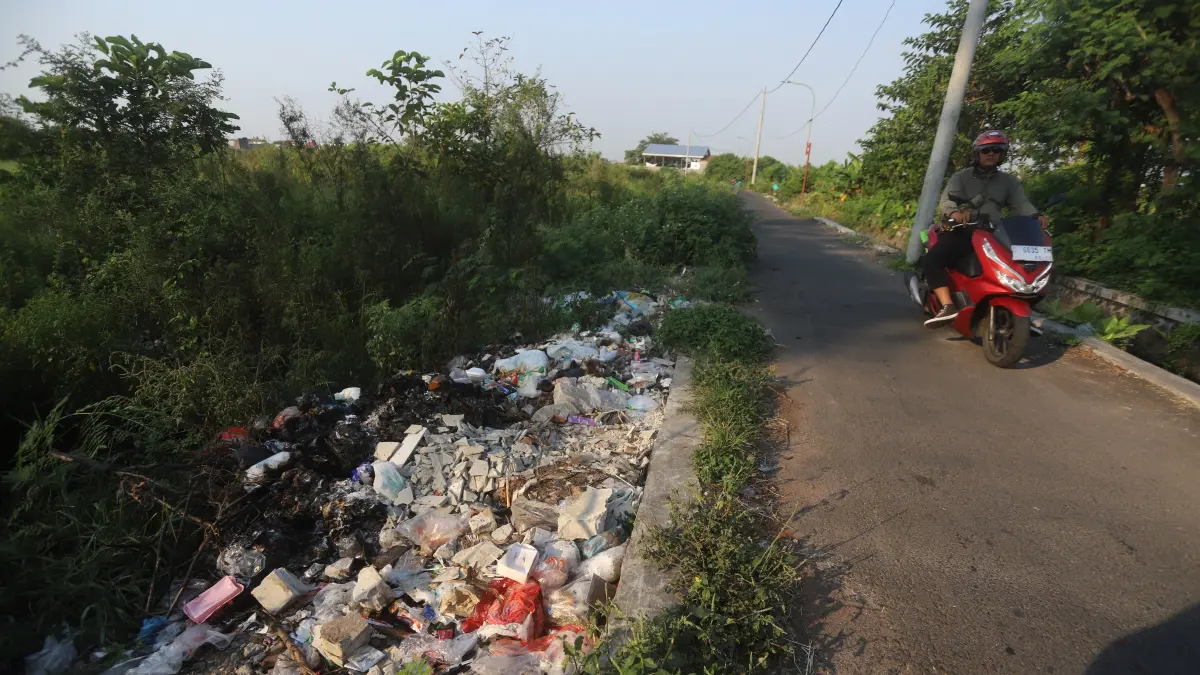 TAK TERURUS: Pengendara motor melintas di Jalan Ken Dedes, Kelurahan Wates, Kecamatan Magersari, Kota Mojokerto, Kamis (2/7). Tampak tumpukan sampah dibuang sekenanya menimbulkan kekumuhan di lokasi. (Sofan JPRM)