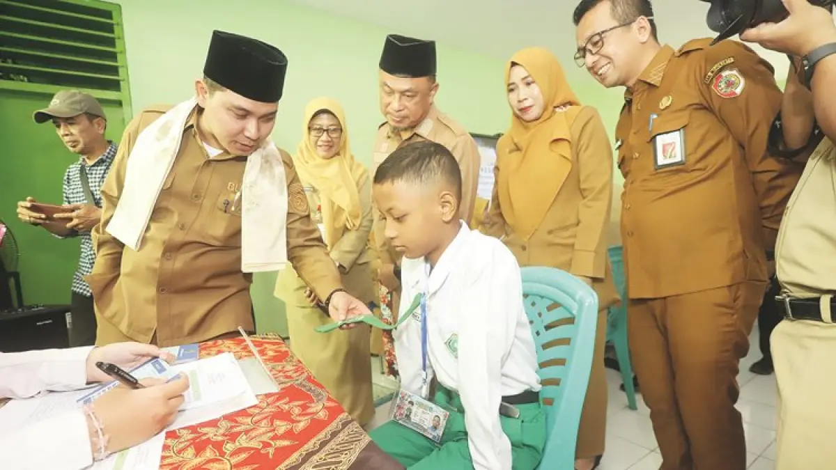 MASIH BERSERAGAM MADRASAH: Bupati Mojokerto Muhammad Albarraa didampingi Kepala Dispendik Kabupaten Mojokerto Amsar Azhari Siregar (kanan) menyapa peserta didik baru saat menjalani pendataan kesehatan di SMPN 1 Sooko, Senin (13/7). (Sofan JPRM)