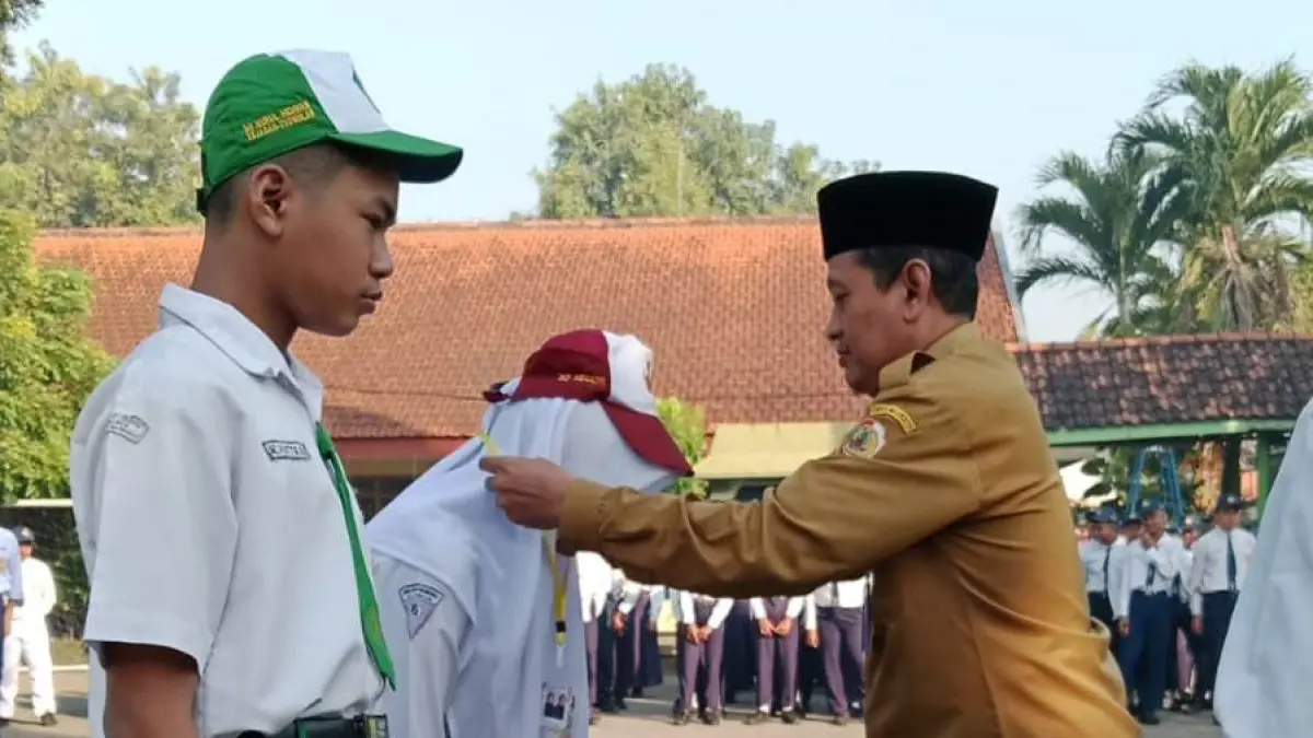 SIMBOLIS: Kepala SMPN 1 Trowulan Hari Widarto menyematkan tanda peserta kepada perwakilan siswa baru sebagai simbol dibukanya kegiatan MPLS Ramah 2026.