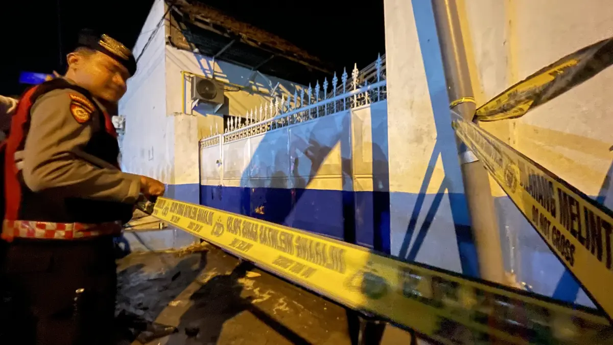 DISELIDIKI: Polisi memasang police line di depan pintu gerbang SPPG Medali 1, Desa Medali, Kecamatan Puri, Kabupaten Mojokerto yang meledak dan ambruk, Kamis (13/8) malam.