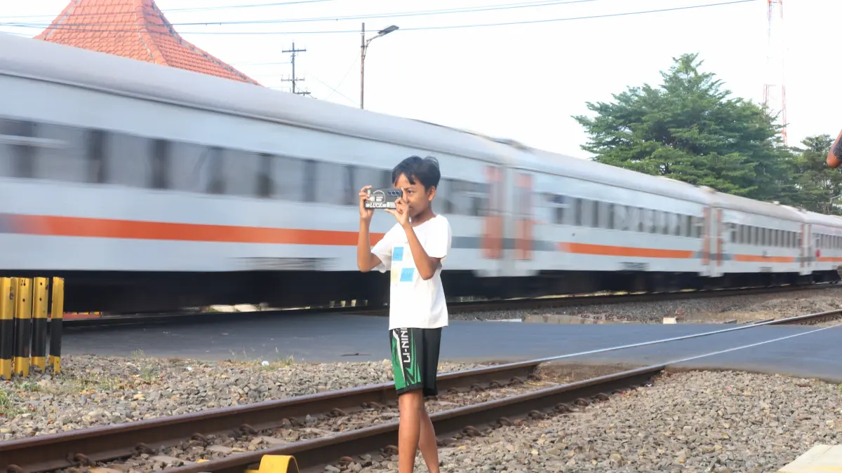 NAIK: Seorang anak mengabadikan kereta yang tengah melintas di perlintasan area Kota Mojokerto, beberapa waktu lalu. Volume penumpang kereta api di Stasiun Mojokerto mengalami lonjakan selama libur panjang Maulid Nabi pekan ini. (Sofan Kurniawan/JPRM)