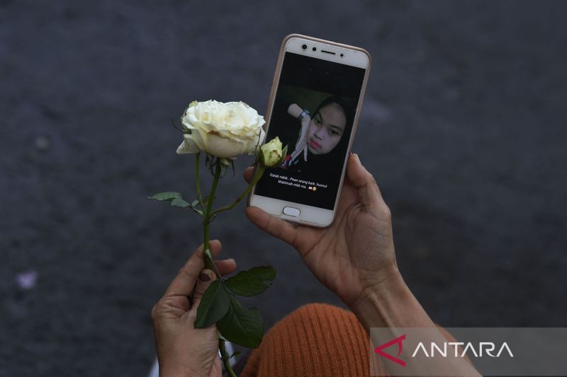 Seorang warga memegang bunga di samping foto korban kerusuhan di Stadion Kanjuruhan, Malang, jawa Timur, Minggu (2/10/2022). Berdasarkan identifikasi dari tim Disaster Victim Identification (DVI) dan Dinas Kesehatan Pemkab dan Kota Malang tercatat 125 ora