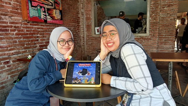 KOMPAK: Aprilia (kiri) dan Lintang (kanan), memamerkan karya digital ”Sepasang Sepatu di Beranda Rumah Ibu”. Karya tersebut dibuat karena terinspirasi insiden tragedi Kanjuruhan. (Indah Oceananda/Jawa Pos Radar Mojokerto)