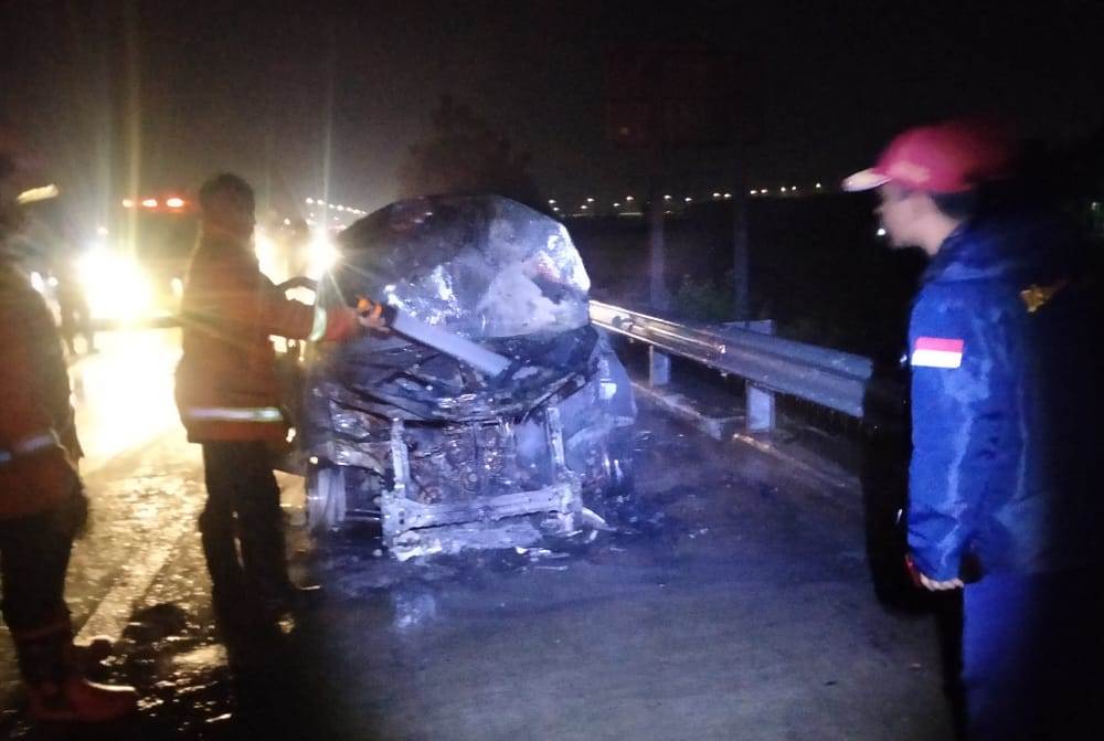 HANGUS TAK TERSISA: Petugas pemadam kebakaran BPBD Kabupaten Mojokerto melakukan pembasahan terhadap mobil Toyota Avanza yang terbakar di tol Jombang-Mojokerto, tepatnya di KM 706+400, Gedeg arah Jombang, Minggu (16/4) malam. (PJR Dirlantas Polda Jatim fo