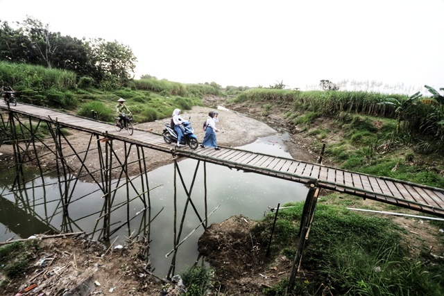 DARURAT: Petani dan pelajar melintasi jembatan darurat dari bambu di Desa Talun, Kecamatan Dawarblandong, Kabupaten Mojokerto, Selasa (6/6). (Sofan Kurniawan/JPRM)