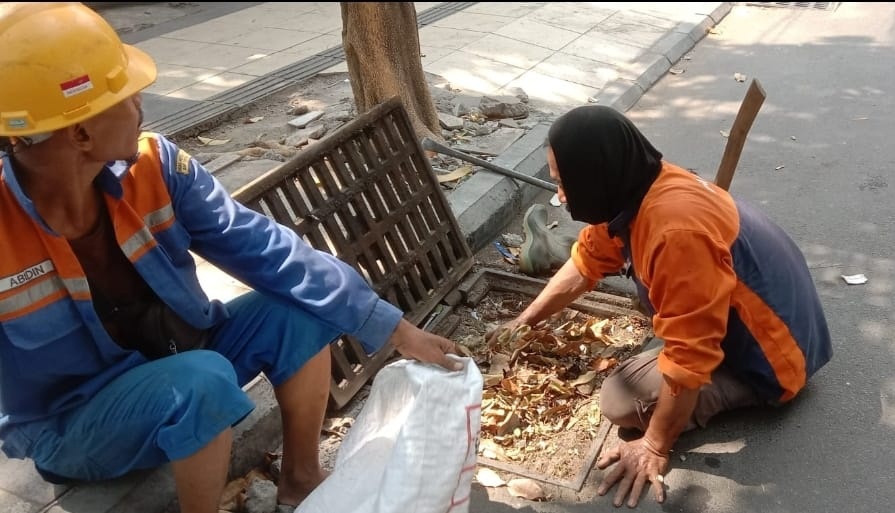 BERSIH-BERSIH: Petugas DCKPKP Gresik saat membersihkan lubang saluran yang tersumbat sampah.
