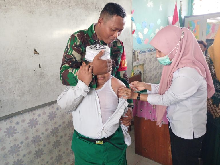 IMUNISASI : Anggota Babinsa Koramil Mengnati Serda Saikhul saat membantu petugas kesehatan Desa Beton, Kecamatan Menganti di Madrasah Ibtidaiyah Roudlotus Shibyan desa Beton Kecamatan Menganti, Gresik