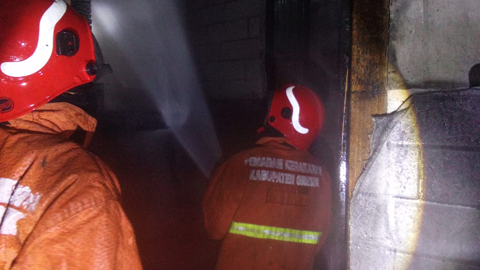 PENYEMPROTAN: Anggota Damkarla Polres Gresik saat melakukan penyemprotan kebaran di sebuah rumah di Jalan Dr. Wahidin Sudirohusodo, Desa Dahanrejo, Kecamatan Kebomas, Gresik.