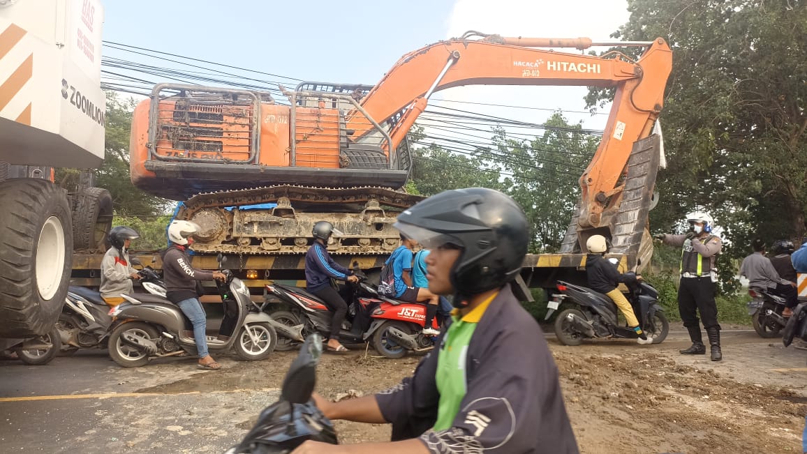 EVAKUASI : Polisi saat melakukan pengaturan jalan saat alat berat eksavator dievakuasi usai alami laka kerja terperosok masuk anak Kali Lamong di Jalan Raya Iker - Iker, Desa Iker - iker Geger
