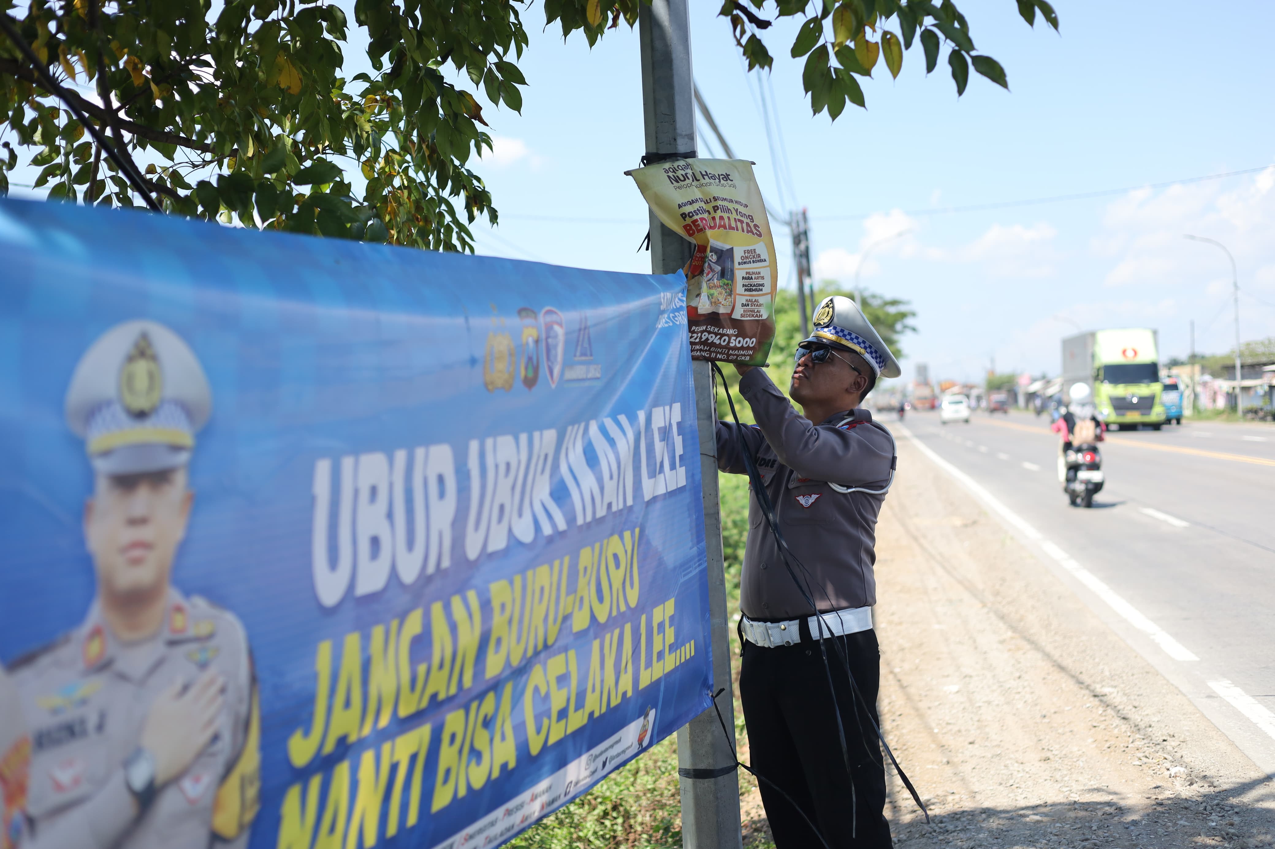 SOSIALISASI KESELAMATAN: Anggota Satlantas Polres Gresik memasang banner imbauan bahaya menyalip dari kiri di sepanjang Jalan Raya Duduksampeyan, Gresik.