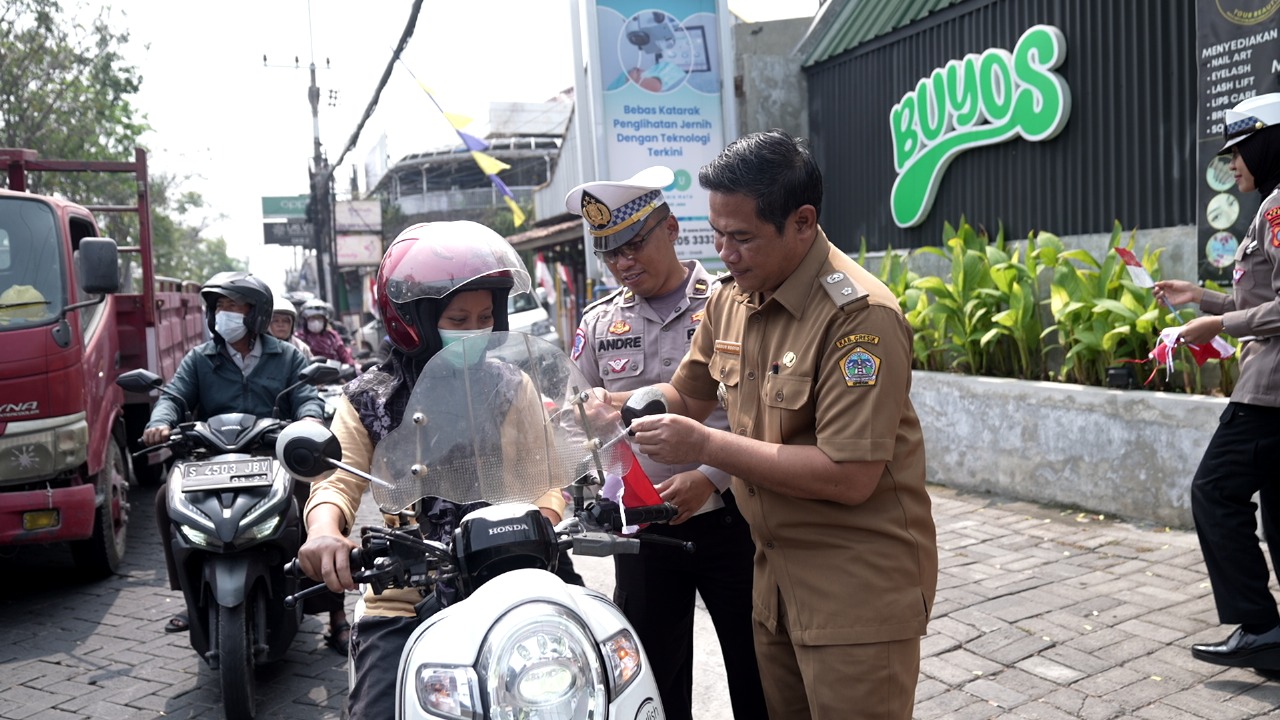 BAGIKAN BENDERA : Kades Yosowilangun Abdur Rosyid bersama Anggota Satlantas Polres Gresik saat membagikan bedera dan pin merah putih kepada pengendara Jalan Raya untuk menyambut hari kemerdekaan.