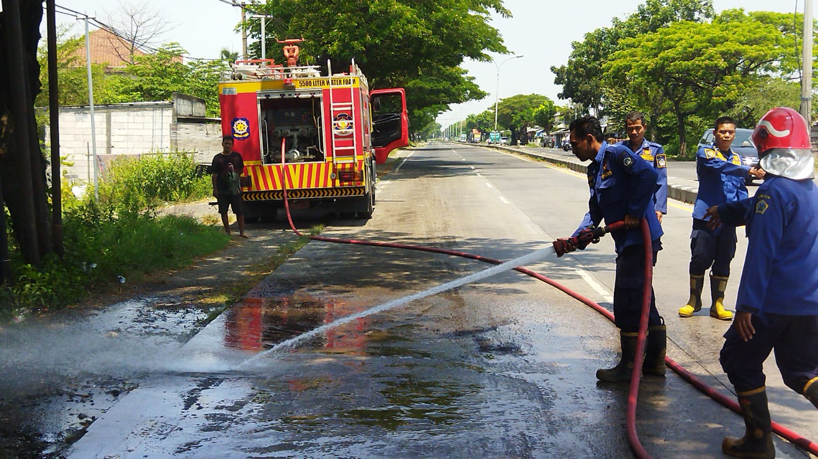 DISEMPROT : Petugas Damkar Gresik saat menyemprot tumpahan Solar di Jalan Duduksampean yang membuat sejumlah pengendara motor terjatuh.