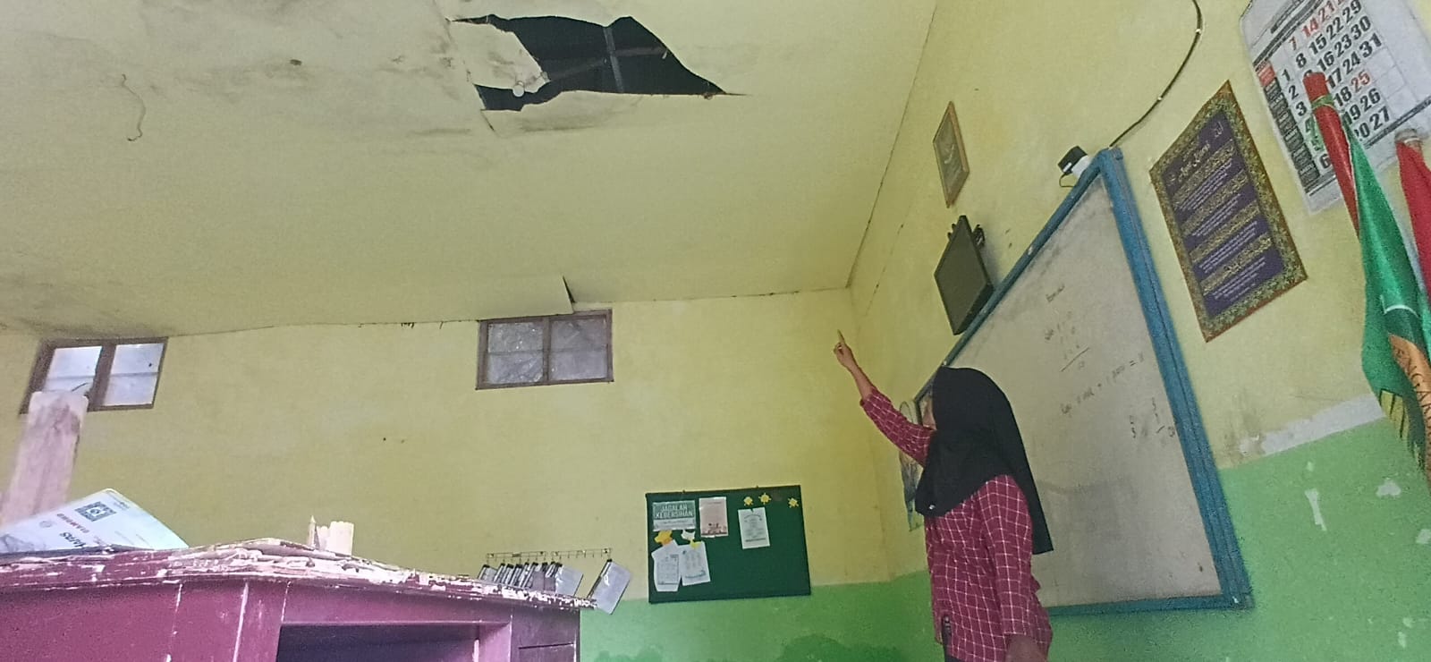 Lihat : Operator Tata Usaha MI Ma&rsquo;arif Ngargosari, Erma Astutik, saat menunjukkan kondisi atap kelas yang rusak dan berlubang.