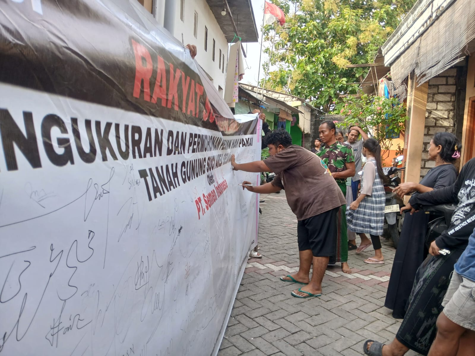 BUKTI: Sejumlah warga Desa Suci membubuhkan tanda tangan di atas kain petisi sebagai simbol penolakan penguasaan lahan oleh perusahaan.