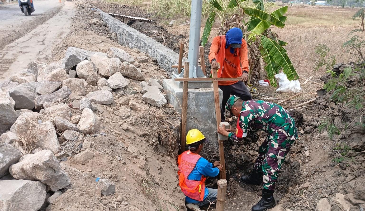 GOTONG ROYONG: Babinsa Koramil Benjeng bersama warga Desa Banter saat melakukan pemasangan pondasi Tanggul Penahan Tanah (TPT).