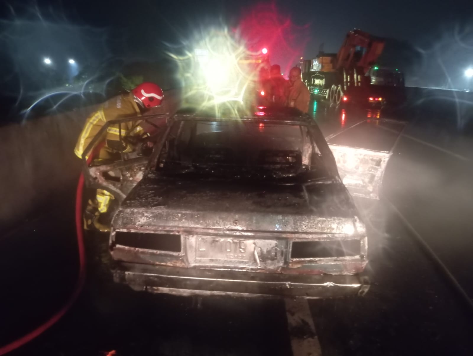 Foto: Istimewa/Radar Gresik PEMADAMAN: Petugas Damkarla Gresik memadamkan mobil sedan Corolla DX bernopol L 1079 I yang terbakar di Tol Surabaya&ndash;Gresik KM 11, dekat rest area Kebomas, Gresik
