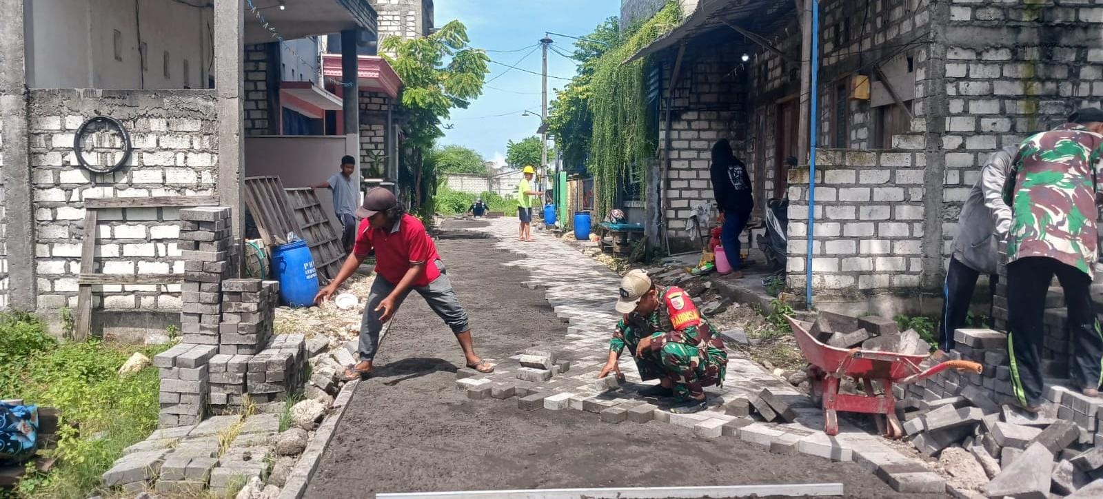 MEMBANTU : Babinsa Manyar membantu langsung pasang paving bersama warga. 