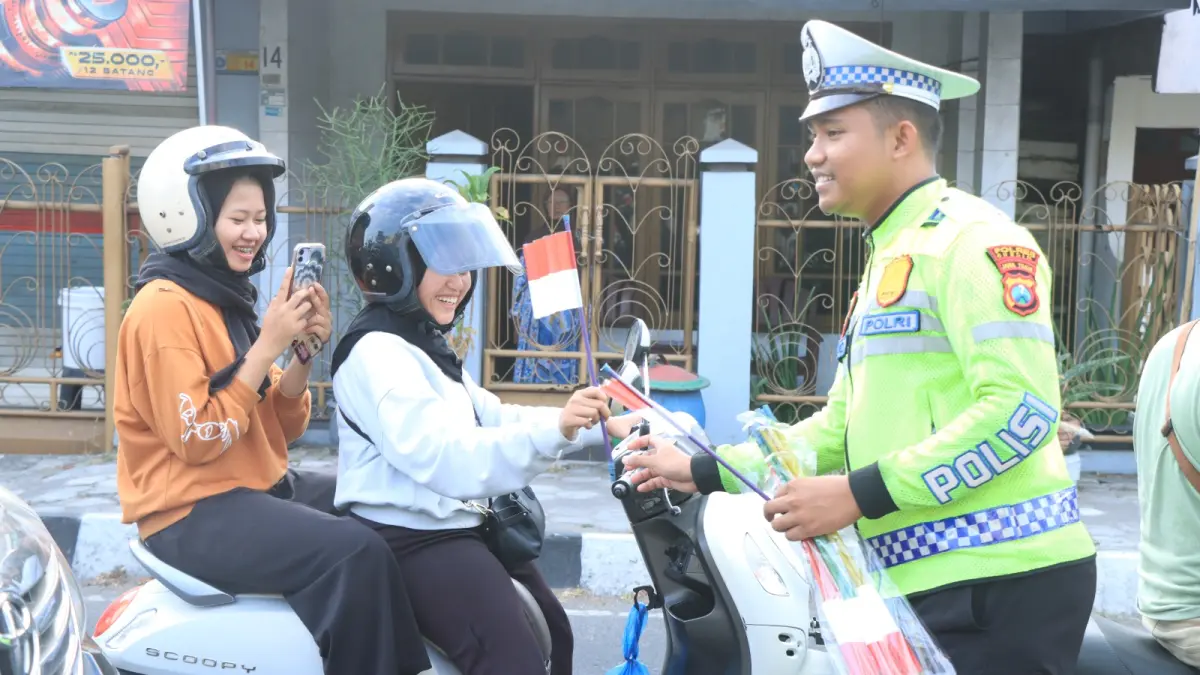 BENDERA : Anggota Polres Gresik saat membagikan bendera merah putih ke pengguna jalan di Simpang Empat Sentolang, Kelurahan Sidomoro, Kecamatan Kebomas, Gresik. (Foto ; Ist/Radar Gresik) 