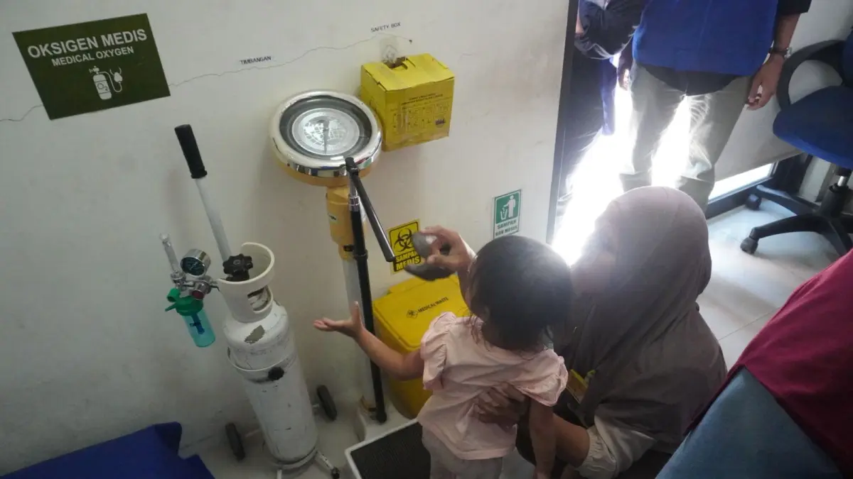 PEMANTAUAN RUTIN: Salah satu balita sedang menjalani penimbangan berat badan di timbangan injak dengan pendampingan ibunya saat kegiatan program Pertamina Sehati. (Foto : Ist/Radar Gresik) 