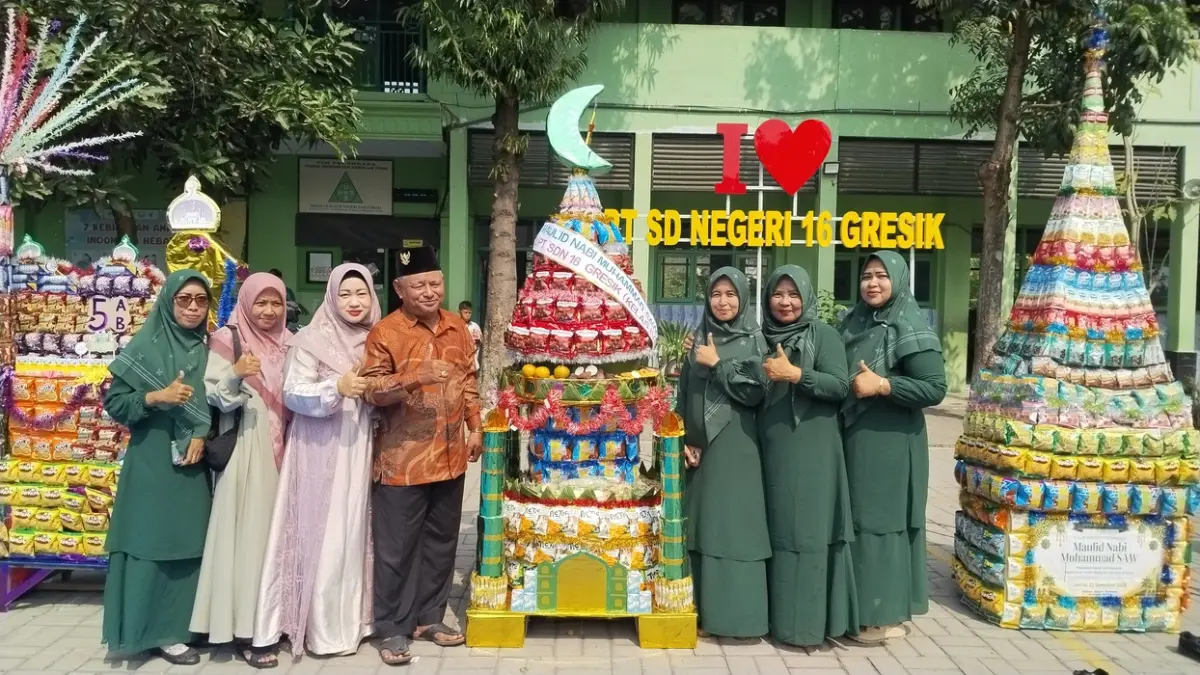 GUYUB RUKUN: Kepala UPT SDN 16 Gresik Naniek Mariawati (kedua dari kanan) bersama Kepala Desa Dahanrejo H. Mochammad Hasan (keempat dari kiri) dan dewan guru berfoto bersama di dekat kreasi gunungan snack. (Foto : Riri/Radar Gresik)