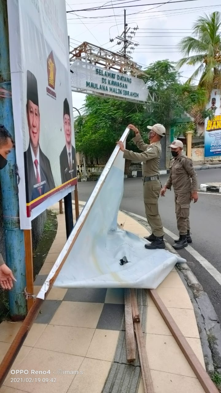 DITURUNKAN: Petugas Satpol PP Gresik yang menurunkan reklame yang rusak yang membahayakan pengguna jalan.