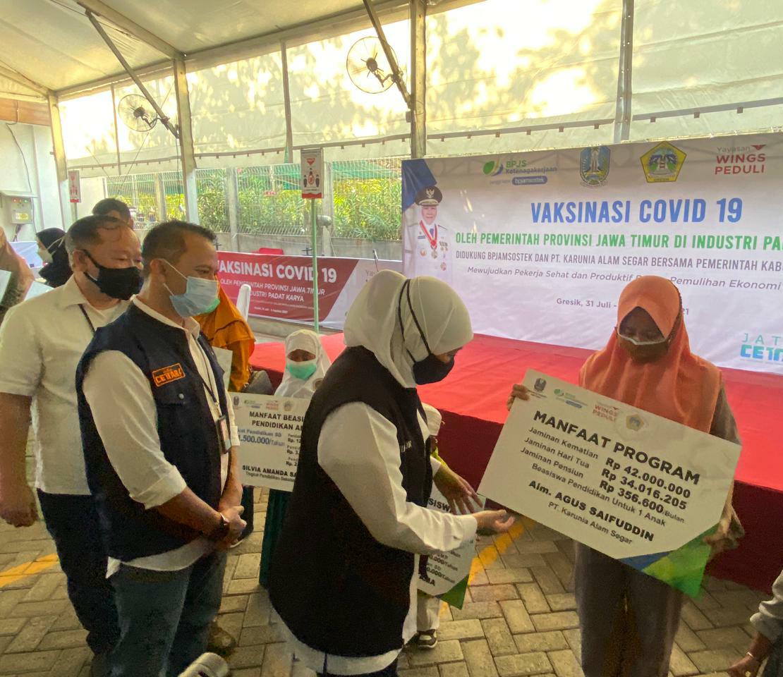 Gubernur Jatim, Khofifah Indar Parawansa didampingi Deputi Direktur Wilayah BPJAMSOSTEK Jawa Timur, Deny Yustulian menyerahkan santunan kepada ahliwaris karyawan PT KAS dalam kegiatan vaksinasi masal. (Firman/Radar Gresik)