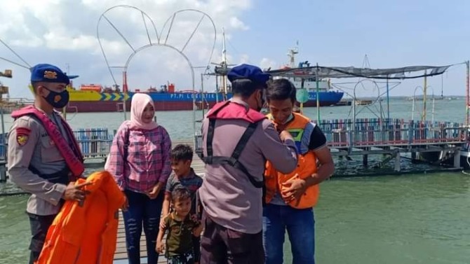 WAJIB PAKAI JAKET PELAMPUNG: Anggota Satpolairud Polres Gresik saat memakaikan jaket pelampung kepada para penumpang perahu wisata yang berada di Kelurahan Lumpur. (Ist/Radar Gresik)