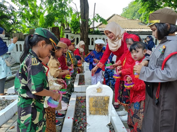 Kepala TK Darul Falah Nor Hidayati bersama murid-muridnya melaksanakan prosesi tabur bunga di makam pahlawan. (Riri/Radar Gresik)
