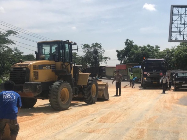 DIBERSIHKAN: Anggota Unit laka Satlantas dibantu warga saat melakukan pembersihan tumpahan jagung usai truk tronton menabrak truk gandeng bermuatan jagung di Jalan Raya Desa Ambeng - ambeng, Kecamatan Duduksampeyan. (Ist./Radar Gresik)