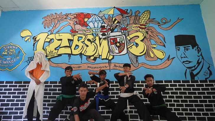 Anggota ekstrakurikuler pencak silat berpose di depan grafiti bertema persatuan dan kesatuan yang dibuat di hampir setiap kelas.