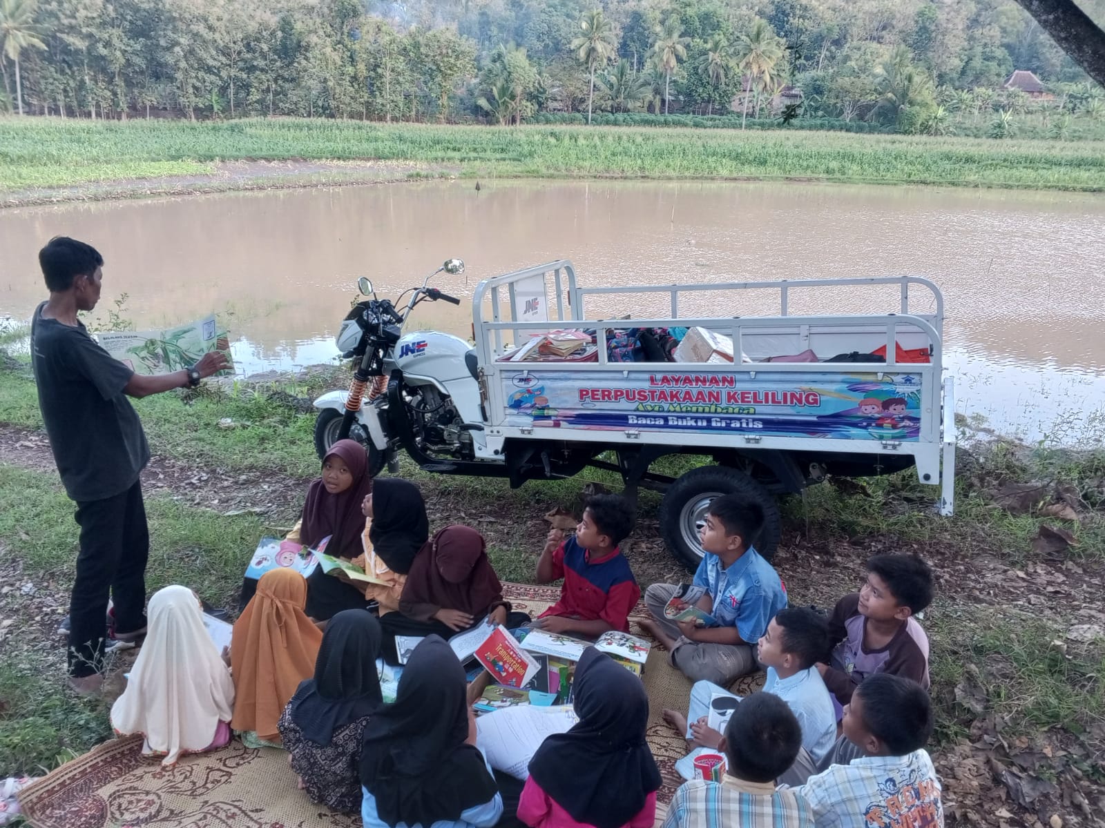 Pendiri Rumah Baca Sang Petualang Wahyudi membawa buku-buku menggunakan motor roda tiga JNE mengajak anak-anak di Desa Tirtosuworo Giriwoyo membaca dan mendongeng di Telaga Simpar.