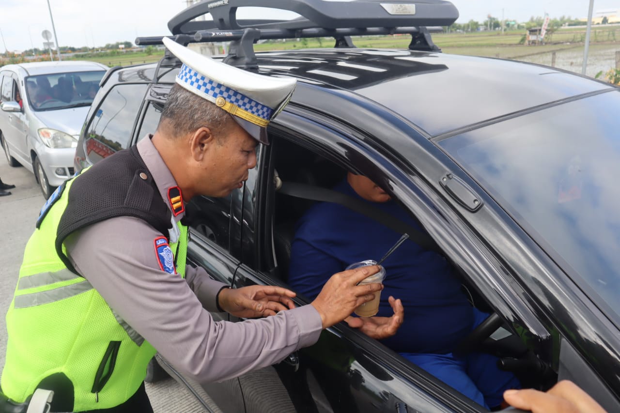 Anggota Polres Sragen membagikan kopi ke pengendara yang melintas di Exit Tol Pungkruk,Sragen dalam rangka Operasi Lilin Candi 2024, Selasa (24/12/2024). (Ahmad Khairudin/Radar Solo)