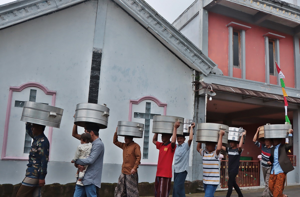 Warga Dusun Sidorejo, Desa Genting, Kecamatan Cepogo, Boyolali membawa tenongan menuju makam dengan melintas gereja setempat, Senin (17/2/2025).